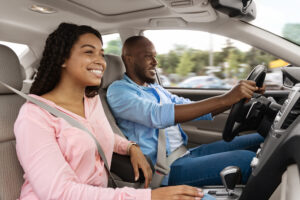 Happy African American man and woman going on summer vacation by car. Beautiful millennial couple sitting inside their new auto, young family cheerfully smiling looking at road, profile side view